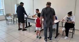 Fotografia colorida em plano médio mostrando o interior de uma seção eleitoral. Eleitores, inclu...