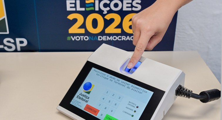 Um dedo feminino está posicionado em um leitor biométrico do terminal do mesário. O leitor emana...