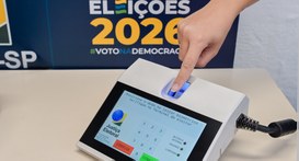 Um dedo feminino está posicionado em um leitor biométrico do terminal do mesário. O leitor emana...