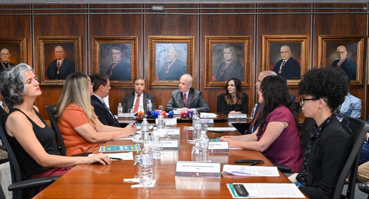 Reunião formal com autoridades e candidatos em trajes sociais dispostas ao redor de uma grande m...