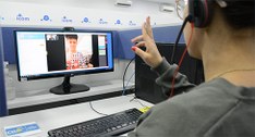 Pessoa intérprete de Libras diante de um monitor se comunica com cidadão surdo.