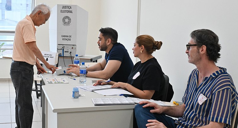 Um homem idoso de cabelos brancos sendo identificado por meio da biometria em uma seção eleitoral