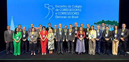 Fotografia de diversas pessoas posando sorrindo em um palco. Os homens vestem terno e as mulhere...