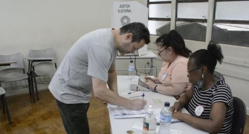Eleições 2024: Como saber se foi convocado para ser mesário ou mesária Eleitor assina caderno de votação em mesa receptora de votos com duas mesárias