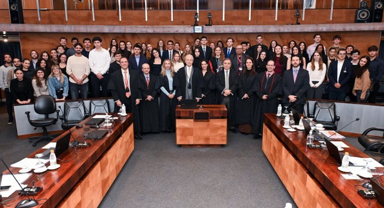 Uma mulher e um homem em trajes formais de pé no plenário do tribunal, com dezenas de estudantes...