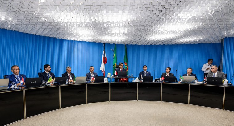 Fotografia de uma reunião formal com homens de terno sentados ao redor de uma grande mesa semici...