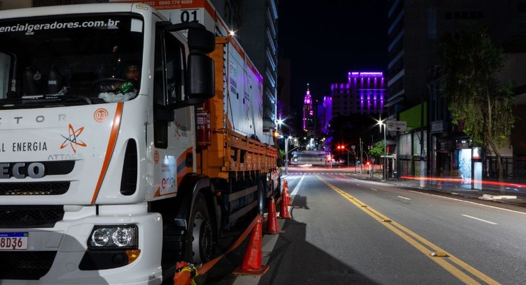 Fotografia noturna em uma rua urbana vazia. Em primeiro plano à esquerda, há um caminhão branco ...