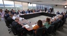 Sala de reunião do TSE com uma mesa quadrada e diversas pessoas sentadas ao seu redor