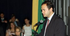 Foto de posse do Juiz André Guilherme Lemos Jorge fazendo seu discurso, com bandeira do Brasil e...
