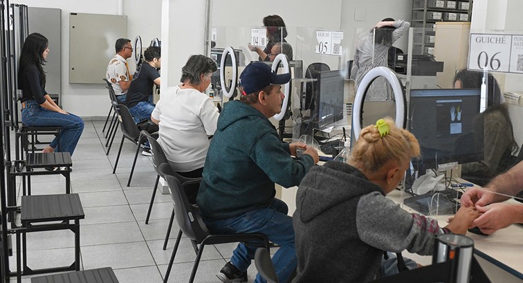 Fotografia do interior de um cartório eleitoral com várias pessoas a ser atendidas em guichês co...