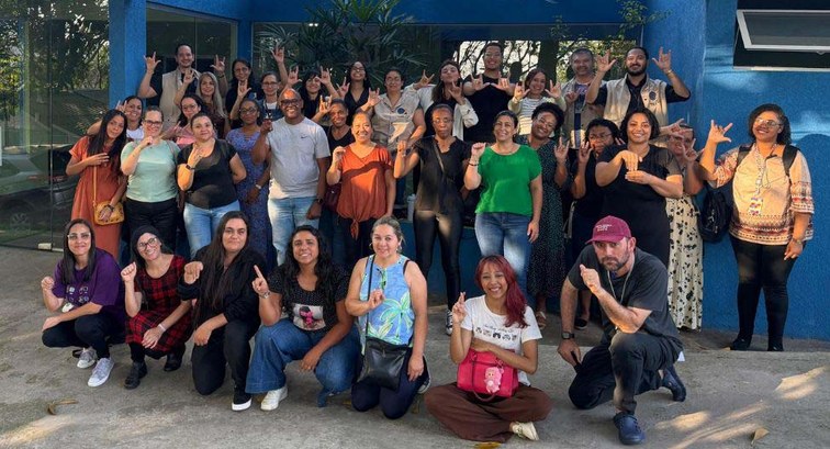 Foto ao ar livre de um grupo de cerca de 30 pessoas diversas, dispostas em pé e agachadas em fre...