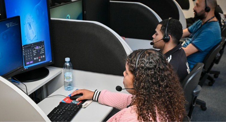 Atendentes de teleatendimento trabalham alinhados em cabines individuais, cada um vestindo heads...