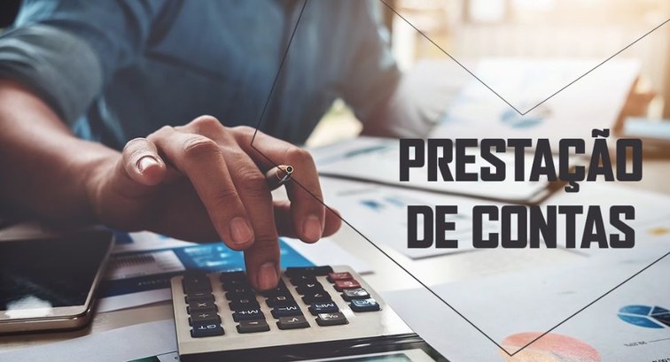 Fotografia em close-up das mãos de uma pessoa digitando em uma calculadora sobre uma mesa de tra...