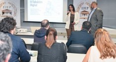 Fotografia em ambiente fechado de uma palestra promovida pela Ejep. Uma mulher fala ao microfone...