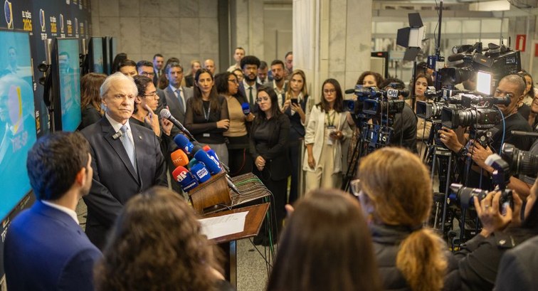 Desembargador Encinas Manfré, de terno e gravata, discursa em um púlpito repleto de microfones, ...