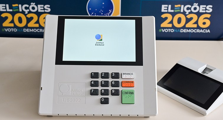 Fotografia de uma urna eletrônica brasileira modelo UE2022 sobre uma mesa, com o terminal do mes...