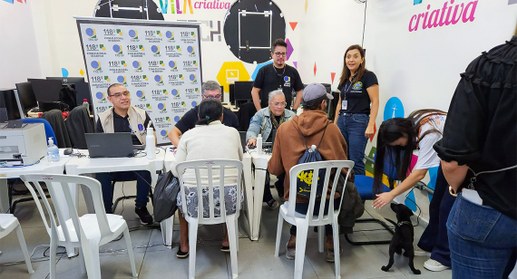 Mesa com servidores da Justiça Eleitoral e pessoas sendo atendidas em mutirão para pessoas em si...