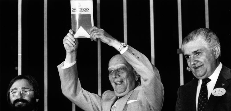 O presidente da Assembleia Nacional Constituinte, deputado Ulysses Guimarães, ergue o primeiro exemplar da Constituição de 1988 Acervo: CEDI/Câmara dos Deputados O presidente da Assembleia Nacional Constituinte, deputado Ulysses Guimarães, ergue o primeiro e...
