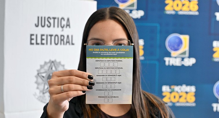 Eleitora segura o papel da "colinha eleitoral" na altura do rosto, cobrindo a boca e o nariz, en...
