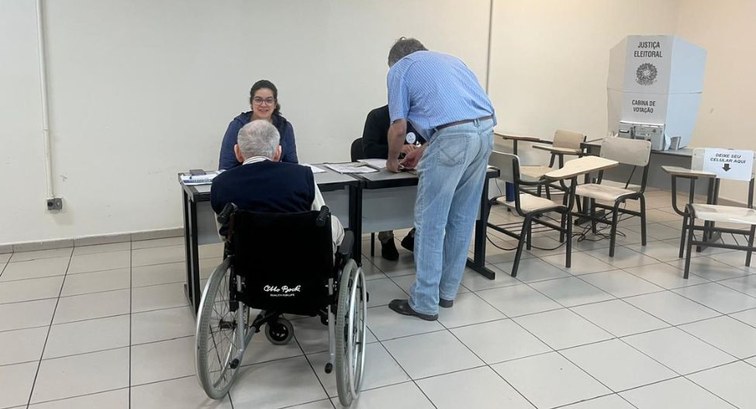 Fotografia de uma seção eleitoral. Visto de costas em primeiro plano, um eleitor idoso em uma ca...
