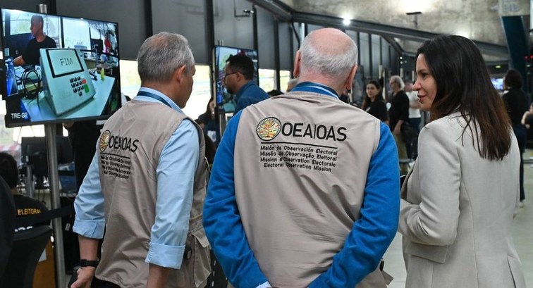 Três observadores internacionais da OEA, vestindo coletes beges identificados com o logotipo da ...