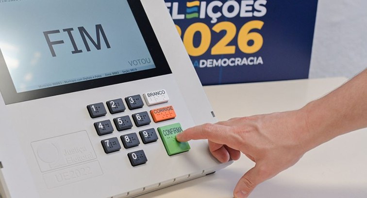 Uma mão pressiona a tecla verde "CONFIRMA" do teclado numérico em Braile de uma urna eletrônica,...